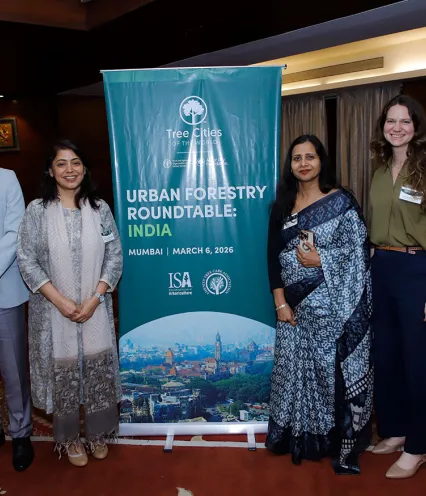 Four individuals pose beside a banner at an event, smiling and engaging with the camera.