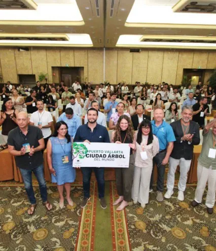 A group of diverse individuals stands together in a room, with a prominent green sign visible in the background.